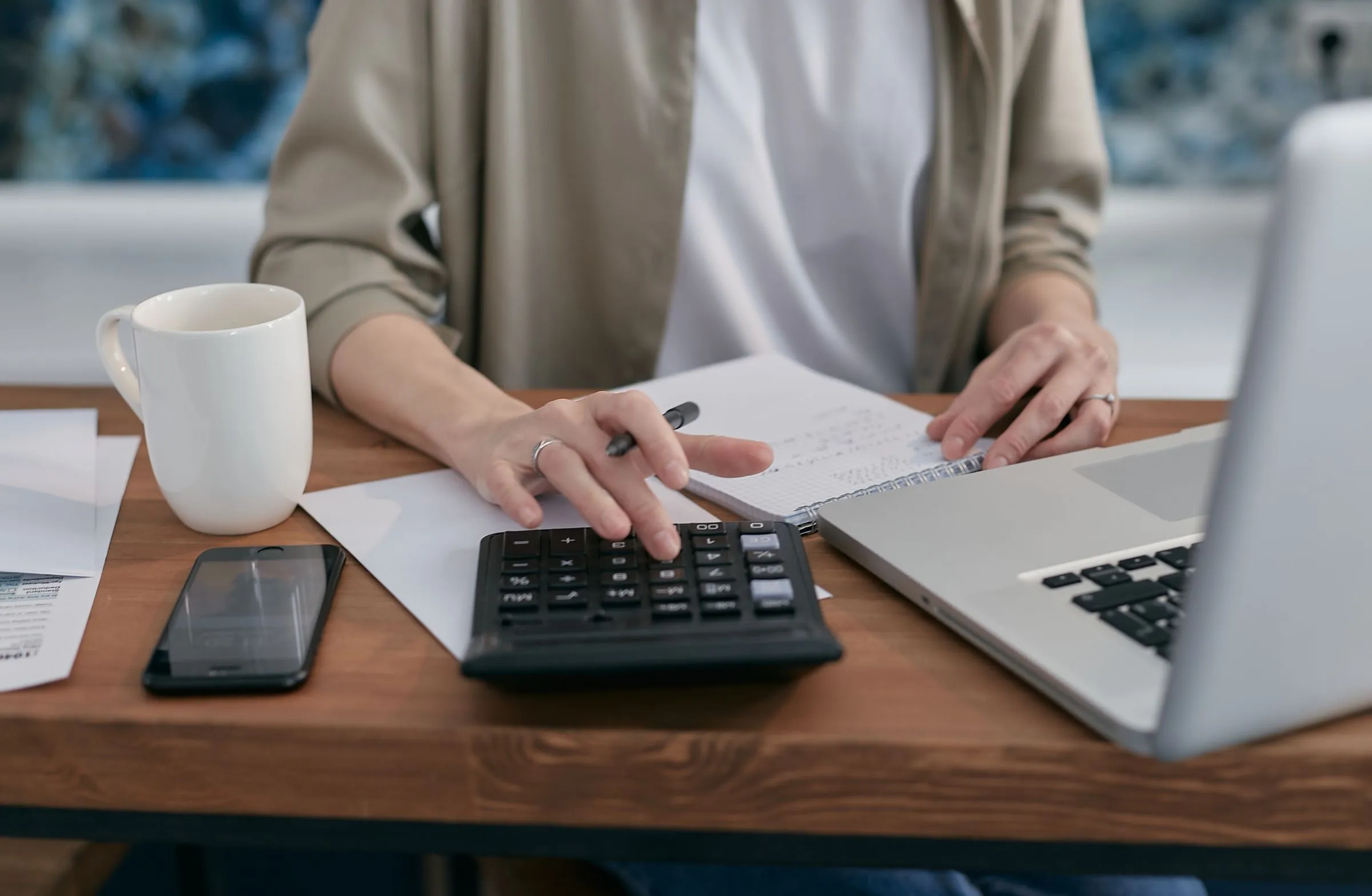 Mains sur une calculatrice, à côté d'un ordinateur portable et d'un carnet