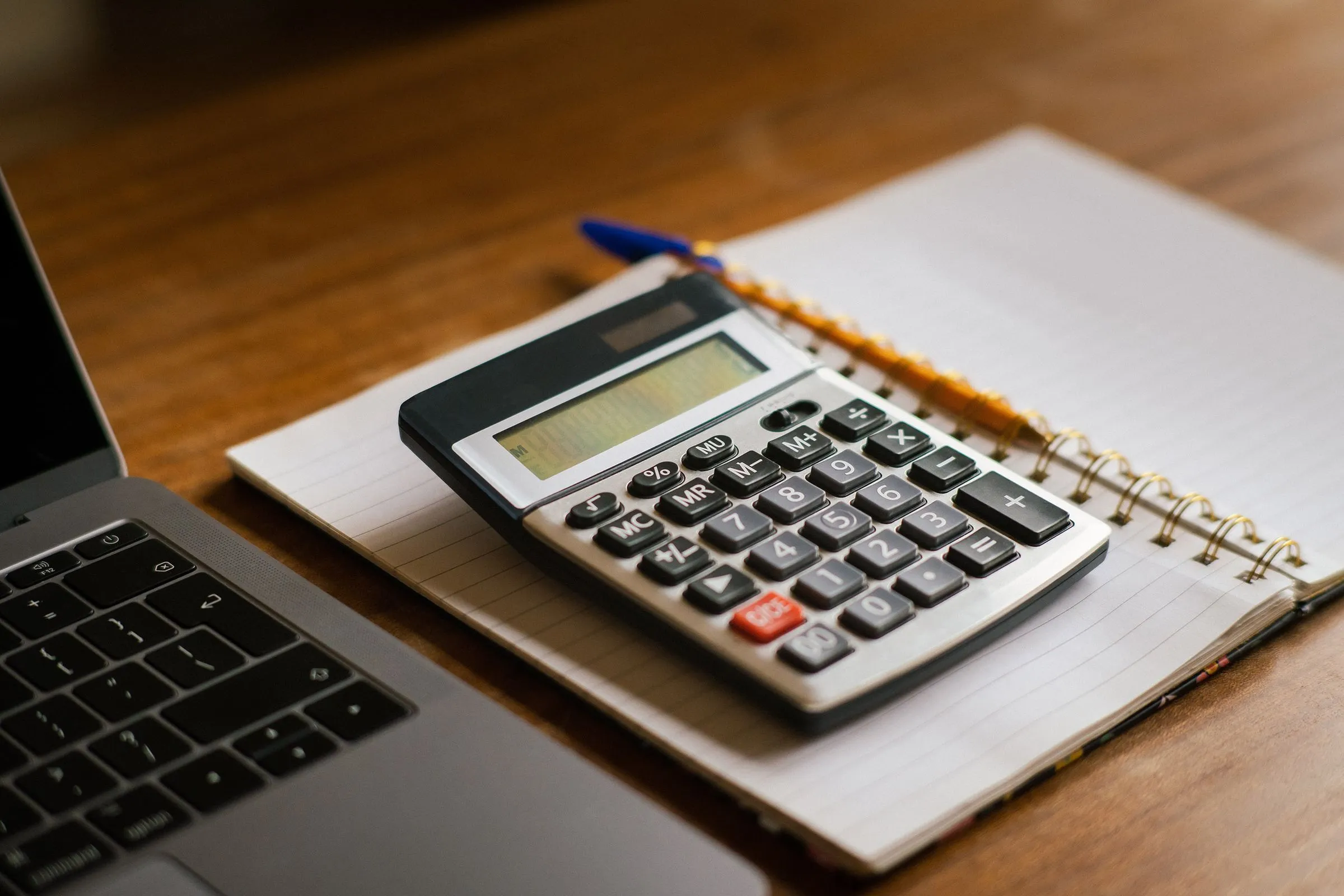 Une calculatrice et un carnet de notes sur un bureau en bois
